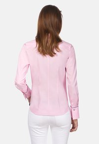 Lichtroze shirt van gladde stof, met lange mouwen en knopenmanchetten, een getailleerd ontwerp en een gebogen zoomdetail.