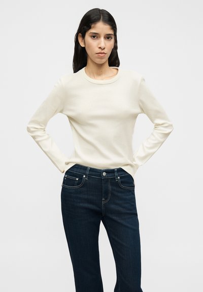 Εκρού πουκάμισο με μακριά μανίκια και στρογγυλή λαιμόκοψη, σε συνδυασμό με σκούρο μπλε τζιν με πέντε τσέπες και κουμπωτό κλείσιμο. Λείο ύφασμα.