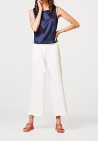 Navy satin sleeveless top, white wide-leg trousers, and coral strappy sandals. Smooth textures and simple silhouettes. Minimalist design.