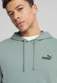 Hoodie vert clair en tissu doux, doté d'une poche kangourou, d'une capuche avec cordon de serrage, et d'un logo Puma noir contrastant sur la poitrine.