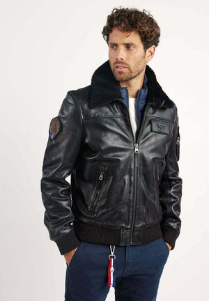 Veste bomber en cuir noir avec un col en fausse fourrure, des poignets et un ourlet côtelés, des poches zippées et des détails de patch brodés.