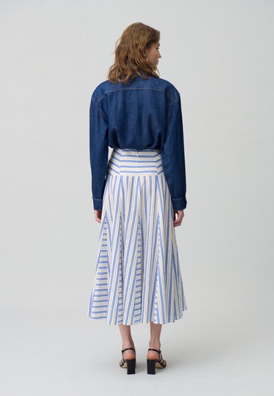 Camisa de mezclilla de manga larga combinada con una falda de largo medio que presenta rayas verticales azules y amarillas, situada sobre un fondo neutro.
