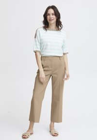 Haut tricoté rayé mint et blanc avec des accents beiges, associé à un pantalon beige sur mesure et des sandales légères. Texture lisse et coupe décontractée.