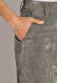 Grau gestreifte Cordhosen mit vertikaler Rippstruktur, elastischem Bund und Seitentasche. Nahaufnahme einer Hand in der Tasche.
