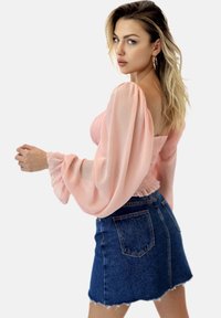 Helles rosa, durchsichtige Bluse mit langen Ärmeln und gerafftem Oberteil, kombiniert mit einem dunklen Denim-Minirock mit ausgefranstem Saum und Gesäßtaschen.