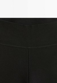 Czarne legginsy z szerokim, miękkim pasem. Tkanina wydaje się gładka i elastyczna, ma prosty krój bez wzorów czy ozdobników.