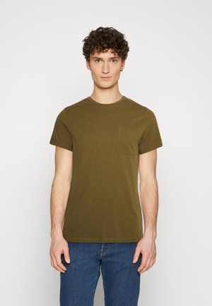 Olivgrünes T-Shirt mit kurzen Ärmeln aus weichem Stoff. Verfügt über eine schlichte Textur und eine Brusttasche. Kombiniert mit blauen Jeans.