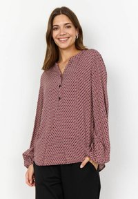 Red and white patterned blouse with a notch collar, long sleeves, and black buttons, paired with black bottoms. Soft fabric texture.