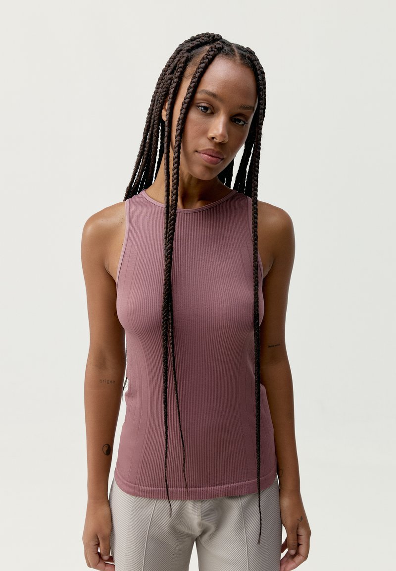 Ribbade, ärmlösa toppar i mjukt mauve-tyg. Har en hög halsringning och en figurnära silhuett som framhäver plaggets eleganta design.