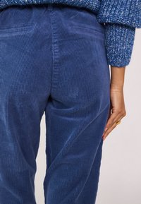 Pantaloni in corduroy blu con una superficie texture a righe, due tasche posteriori e una vestibilità comoda, abbinati a un maglione blu lavorato a maglia.