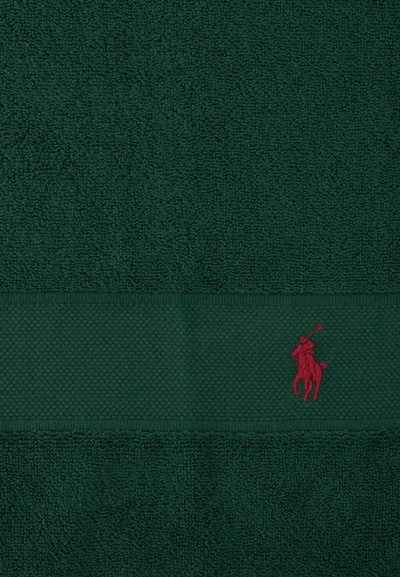 Σκούρα πράσινη πετσέτα με υφή και οριζόντια λωρίδα που φέρει μικρό κόκκινο κεντητό λογότυπο αλόγου με παίκτη πόλο στη δεξιά πλευρά.