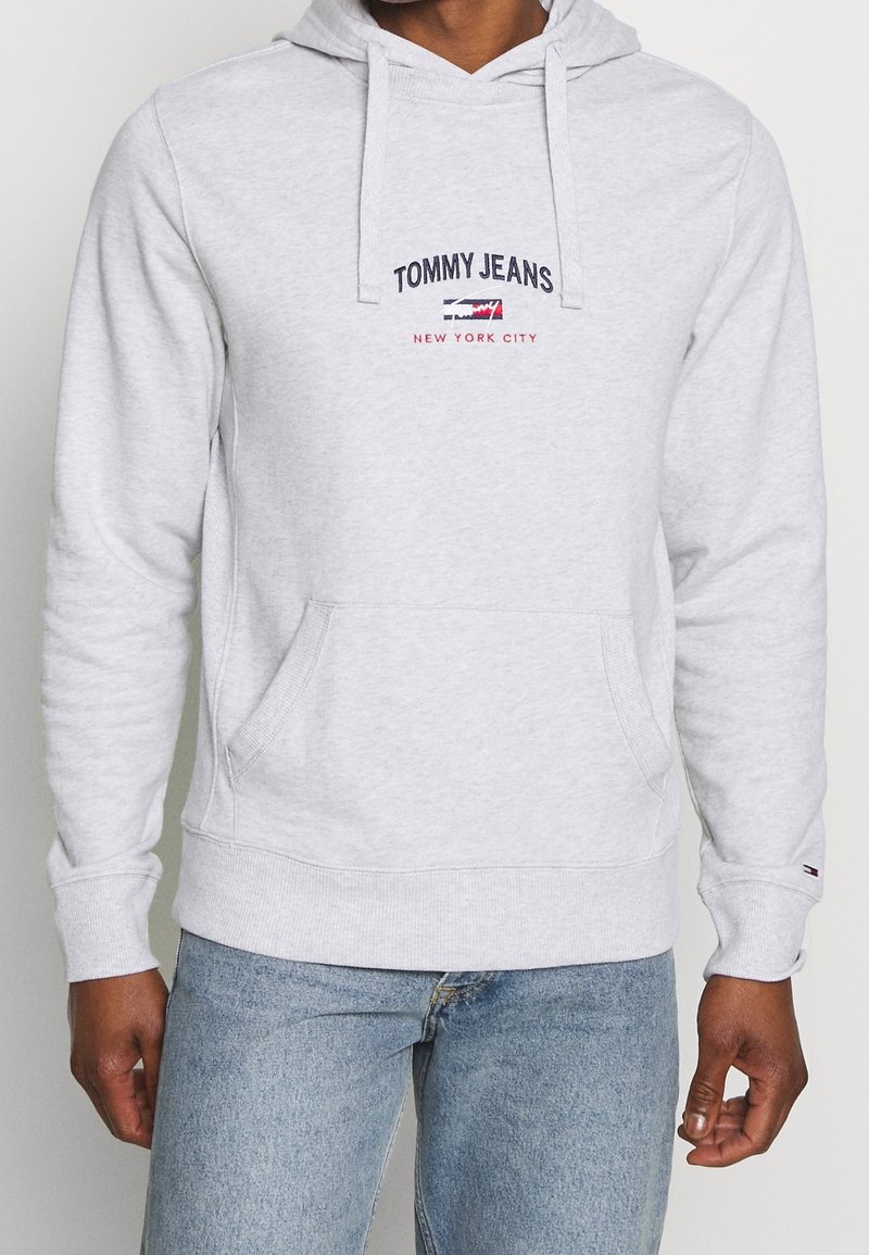 Sweat à capuche gris clair avec poche avant et cordons, logo "Tommy Jeans New York City" sur la poitrine, porté avec un jean bleu clair.