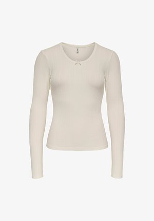 Long-sleeve top in soft cream ribbed fabric, featuring a round neckline and a small white bow accent at the chest.