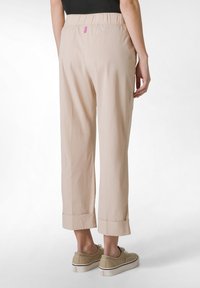 Beige, kevyet, joustavat vyötäröhousut, joissa on käänteet. Takana on pieni, vaaleanpunainen logo. Yhdistetty beigen värisiin kenkiin.