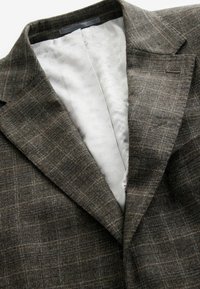Grau karierter Blazer aus strukturiertem Stoff. Das Innenfutter besteht aus einem glatten, hellen Material. Maßgeschneiderte Revers und eine Brusttasche.