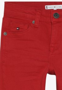 Punaiset farkut, joissa on etutasku, pieni Tommy Hilfiger -logotägi kolikkotaskussa ja brändättävä nappikiinnitys vyötäröllä.