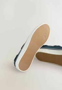 Mørkeblå lærreds sneakers med hvid gummisål og struktureret brun indersål. Har dobbelt spænde detaljer og en glat, afrundet form.