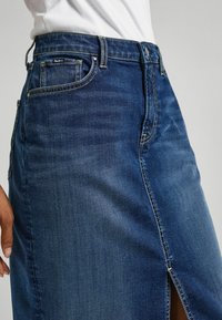 Denim skirt in dark blue with a side slit, featuring a classic five-pocket design and contrasting stitching at the seams.
