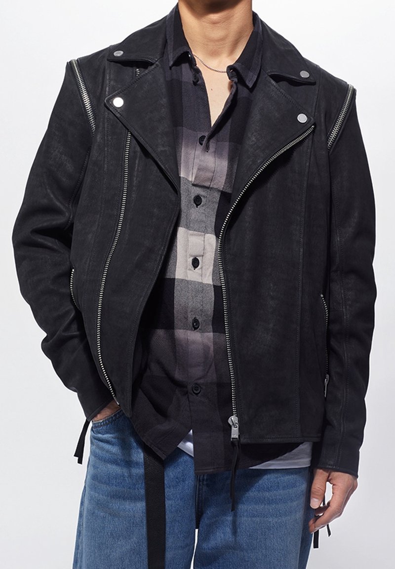 Černá kožená moto bunda se stříbrnými zipy a patentkami, s volnějším střihem a vrstvená přes šedou kostkovanou košili.