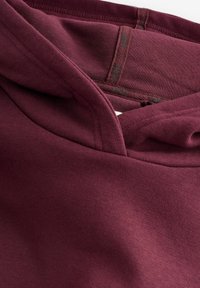 Primo piano del tessuto del felpa bordeaux che mostra i dettagli della cucitura del cappuccio e della fodera interna.