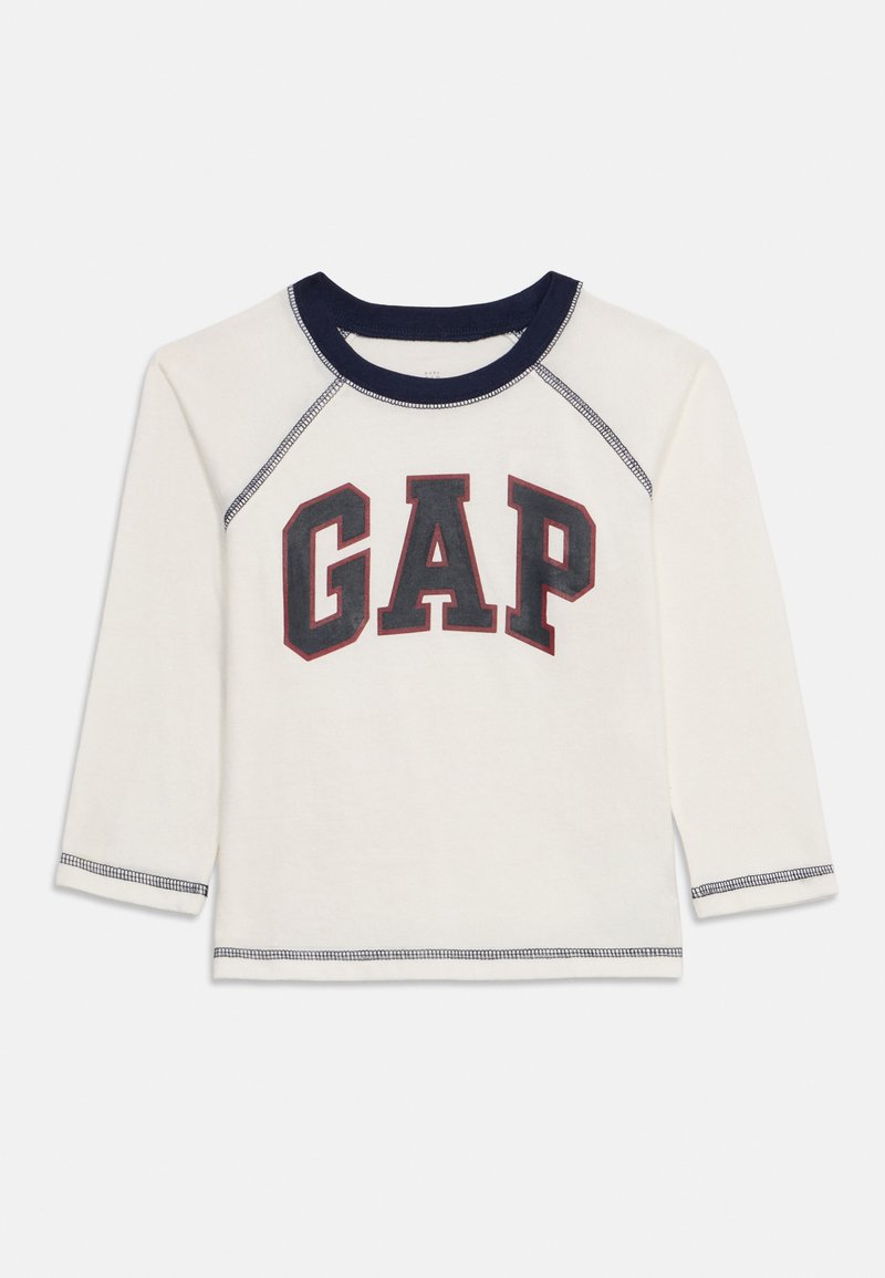 Camisa de manga larga blanca para niño pequeño con cuello azul marino, costuras azul marino y un gran logo "GAP" en rojo oscuro y negro en el frente.