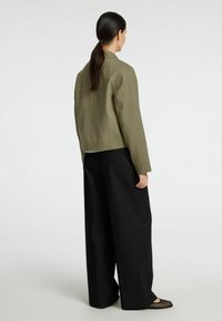 Chaqueta verde oliva recortada con pantalones negros de pierna ancha y recta. La chaqueta tiene un diseño simple, mientras que los pantalones presentan una textura suave.