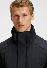 Black high-collar jacket featuring a textured finish, padded design, and structured shoulders, providing a modern and functional appearance.