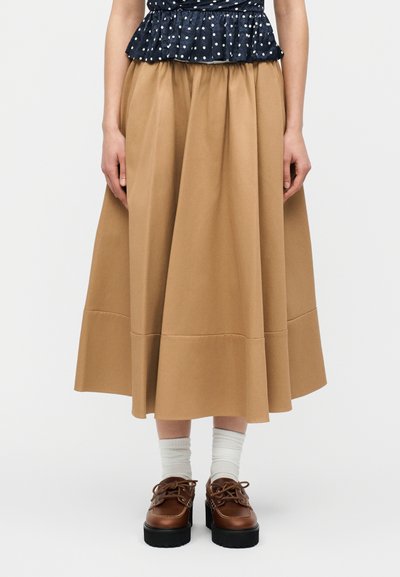 Γυναίκα που φοράει ταμπά midi φούστα, λευκές κάλτσες, καφέ παπούτσια πλατφόρμα με κορδόνια και μπλε σκούρο πουκάμισο με πουά και βολάν στη μέση.