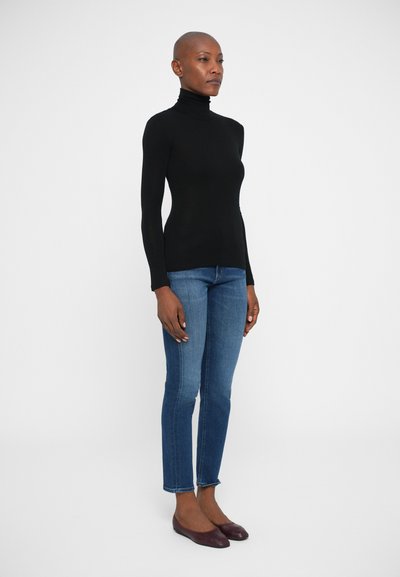 Maglione a collo alto nero realizzato in tessuto morbido, abbinato a jeans slim-fit blu e ballerine borgogna. Design semplice con una silhouette aderente.