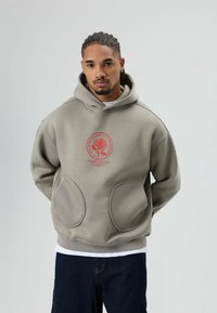 Sweat à capuche gris avec un motif graphique avant représentant une rose entourée de texte, doté de grandes poches avant et d'une coupe décontractée.