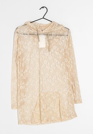 Felpa leggera beige chiaro traslucida con ricami floreali, maniche lunghe e tasca frontale. Il tessuto è leggero, con una texture morbida e dettagli delicati.