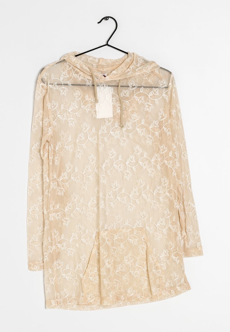 Felpa leggera beige chiaro traslucida con ricami floreali, maniche lunghe e tasca frontale. Il tessuto è leggero, con una texture morbida e dettagli delicati.