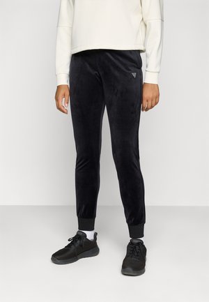 Partie inférieure du corps d'une personne portant un pantalon de jogging noir slim, des chaussettes blanches, des baskets noires et un haut blanc à manches longues.