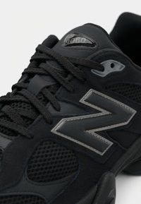 Botte de sport noire avec des matériaux en mesh et en daim, lacets ronds, un logo réfléchissant gris et une semelle en caoutchouc aux bords arrondis.