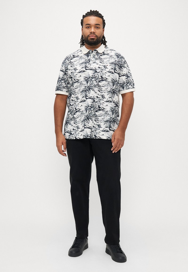 Weißes Polohemd mit kurzen Ärmeln und schwarzem Palmenblatt-Muster, schwarze Hose und schwarze Sneakers. Mit klassischem Kragen und kontrastierenden Ärmelbündchen.