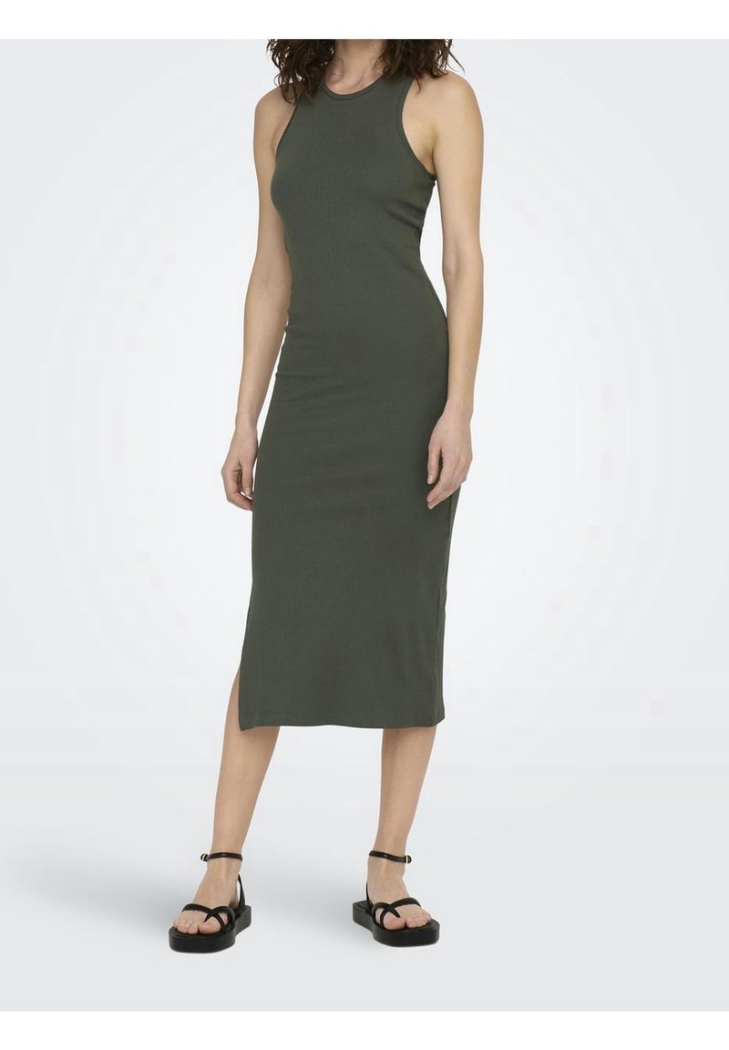 Femme portant une robe midi sans manches vert foncé côtelée et des sandales à plateforme noires, debout devant un fond clair uni