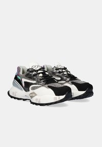 Par de zapatillas chunky con malla en negro, blanco y plateado metálico, cordones negros y suela con patrón, mostradas contra un fondo gris claro liso.