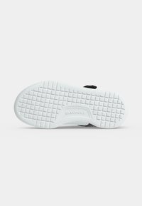 Σόλα ενός λευκού σανδαλιού Skechers με σχέδιο πέλματος σε μονόχρωμο ανοιχτό φόντο.