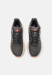 Zapatillas deportivas negras con parte superior texturizada, suela beige, detalles en naranja y cordones negros. Cuenta con un cuello y lengüeta acolchados.