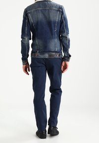 Jeansjacka i mörkblått med en blekt design, med en krage i fuskpäls och tryckknappar. Kombinerad med marinblå byxor och svarta sneakers.