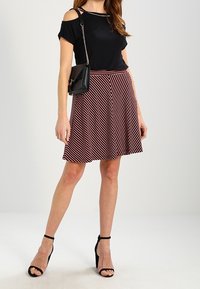 Černý top s odhalenými rameny a krátkými rukávy, v kombinaci s červenou a bílou pruhovanou skater sukní. Černé sandály na podpatku a malá černá kabelka.