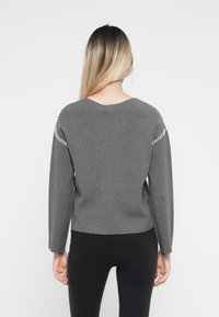 Gray sweater with a V-neck and long sleeves, featuring decorative white stitching along the shoulder seams and a textured finish.