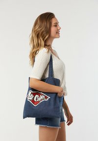 Denim-Tragetasche mit rotem und weißem "Lee Cooper"-Logo; ausgestattet mit doppelten Schulterriemen und strapazierfähigem Stoff in Dunkelblau.