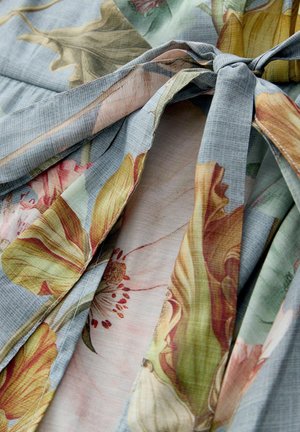 Lilleline kangas, millel on sinakas-halli taust, suured kollased ja roosad lillmustrid, sile tekstuur ning vöökohal seotud lips.