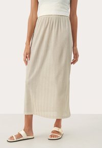 Jupe midi beige clair avec des rayures verticales et une taille élastique. Portée avec des sandales blanches à glisser ornées d'un accent doré.