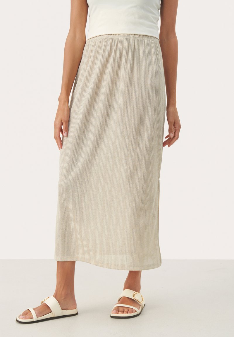Jupe midi beige clair avec des rayures verticales et une taille élastique. Portée avec des sandales blanches à glisser ornées d'un accent doré.