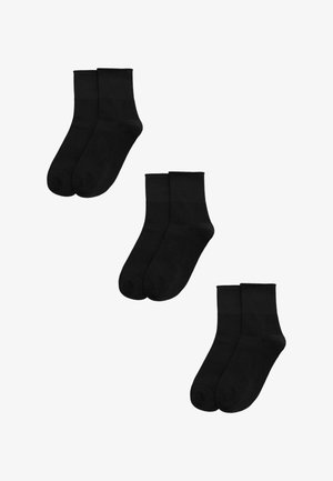 Tres pares de calcetines tobilleros negros lisos dispuestos sobre un fondo blanco.