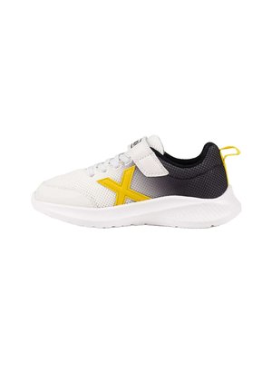 Zapatilla deportiva blanca y negra con logotipo X amarillo, cordones y tira de velcro, y suela blanca texturizada.