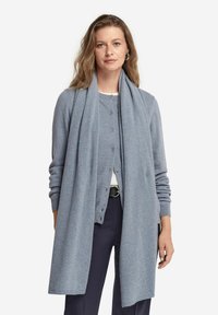 Lyseblå cardigan med knaplukning, lange ærmer og et matchende tørklæde hængende over. Blød tekstur, minimalistisk design, lagdelt over en hvid top.