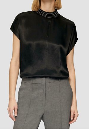 Zwarte satijnen blouse met een hoge kraag en zilverkleurige details. Korte mouwen en een losse pasvorm. Gecombineerd met grijze, op maat gemaakte broek.